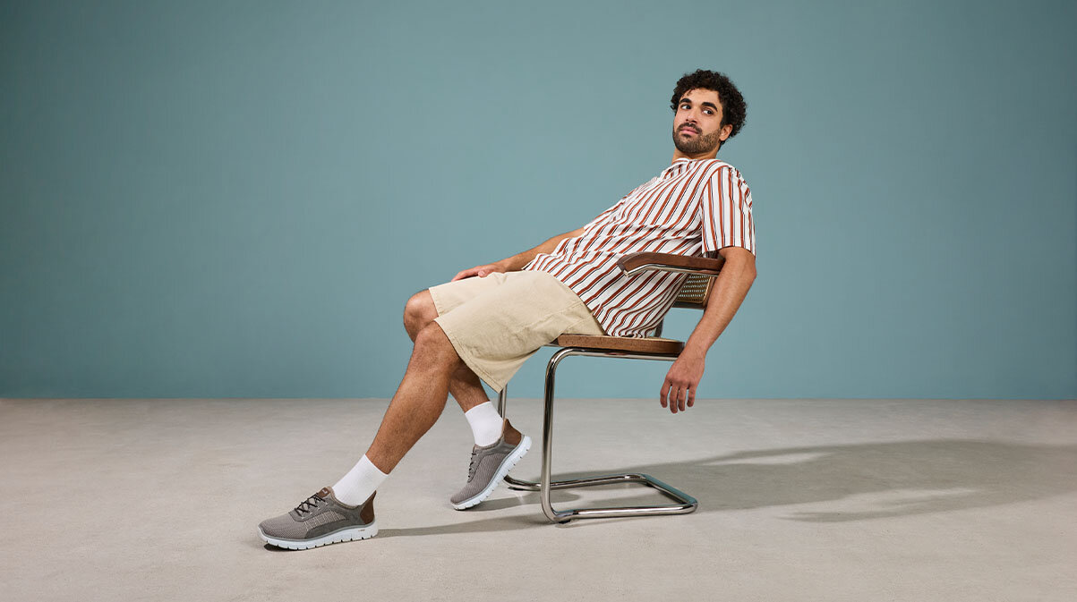 En man som sitter ner i en stol och har på sig ett par gråa sneakers från Rieker